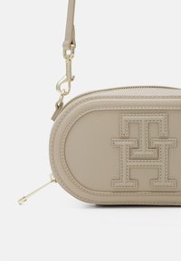 Beige leather crossbody bag with embossed logo, oval shape, gold hardware, and zipper closure. Features a detachable shoulder strap.