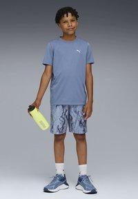 Camiseta azul de manga curta para exercício, calções com padrão, ténis azuis e uma garrafa de água amarela. Logotipo Puma notável na camisa e na garrafa.