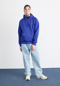 Blue hoodie with a drawstring and front pocket, paired with light blue loose-fitting jeans and yellowish sneakers. Simple design, soft texture.