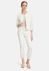 Biała dżinsowa kurtka z srebrnymi guzikami, rękawami do trzy czwarte i zdobieniami w formie dziurek. Połączona z białymi spodniami o kroju 7/8 z podobnymi akcentami.
