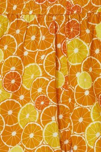 Orange fabric featuring a pattern of overlapping citrus slices in shades of orange, yellow, and white. Smocked waistband detail.