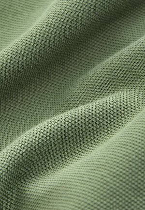 Gewebter grüner Stoff mit feinem, gestricktem Muster, der sich weich anfühlt und eine leicht matte Oberfläche aufweist.