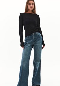 Sort tekstureret langærmet top med bådsnit kombineret med brede blå denimjeans. Begge beklædningsgenstande har en afslappet pasform.