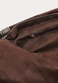 Intérieur d'un sac en daim marron avec une texture lisse, comprenant une poche zippée et un tirette en métal argenté.