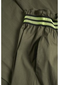 Tela verde oliva con cintura fruncida, que presenta una banda elástica de rayas negras y verdes neón. Textura suave y diseño ligero.
