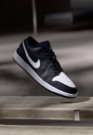 Basket Nike noir et blanc avec lacets flottant au-dessus d'un banc en pierre, prise en faible lumière avec des ombres en arrière-plan.