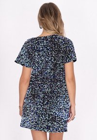 Vestido negro con mangas cortas, cubierto de lentejuelas multicolores que crean un patrón brillante, de corte corto y con una superficie texturizada.