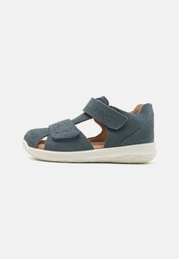 Blå semsket sandal med lukket tå, utskårede sider og to justerbare borrelåsremmer. Har en hvit gummisåle og subtile sømdetaljer.