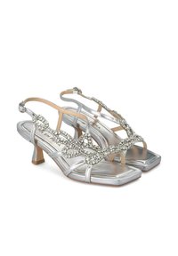 Zilveren sandalen met hakken hebben een glanzende metallic afwerking, een open teen ontwerp, versierde banden met ingewikkelde rhinestone details en een hak van gemiddelde hoogte.