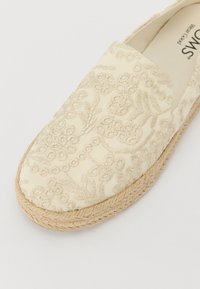 Krémové espadrilky s detailným zlatým vyšívaním, okrúly špička a jútová podrážka. Hladký textilný povrch, ľahký dizajn.