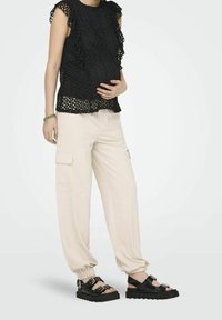 Top in pizzo nero con ricami, abbinato a pantaloni cargo crema con tasche laterali, e sandali neri chunky con dettagli di fibbia.