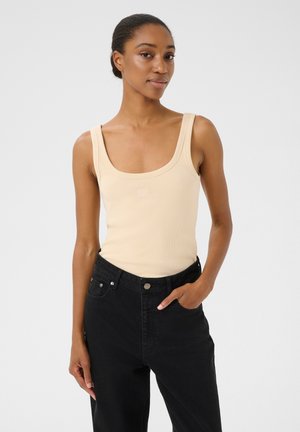 Débardeur beige à côtes avec un décolleté carré et des bretelles larges, associé à un jean noir taille haute avec des poches avant.