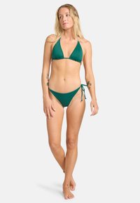 Žalias bikinis, kuriame yra trikampio formos liemenuokas su plonomis petnešėlėmis ir žemas kelnaitės su reguliuojamomis raištelėmis šoninėse, pagamintas iš lygaus, elastingo audinio.