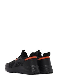 Baskets de sport noires avec un tissu texturé, accents orange sur le talon, languettes, et une semelle en caoutchouc robuste. Design léger pour le confort.