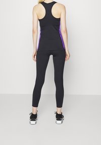 Svart atletisk linne med lila sidokanter, parat med svarta tights. Slitstyg, elastisk; racerback-design; figurnära siluett.