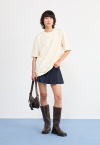 Kremfarget oversized T-skjorte med "adidas"-logo, kombinert med en marineblå miniskjørt. Brune skinnstøvler til kneet og en liten mørk veske fullfører antrekket.