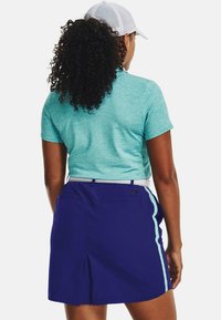 Haut turquoise à manches courtes avec un col rond, associé à une jupe-short violette avec un accent blanc et des bandes latérales. Tissu texturé, coupe décontractée.