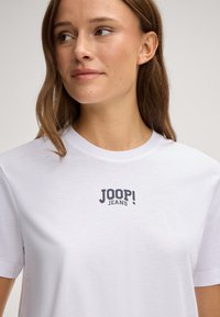 Weißes Baumwoll-T-Shirt mit einem dunkelblauen "JOOP! JEANS"-Logo auf der Brust. Kurze Ärmel und klassischer Rundhalsausschnitt.