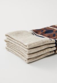 Knit socks stacked horizontally, featuring a cream base with a patterned brown and navy design near the top. Soft texture and elastic cuff.