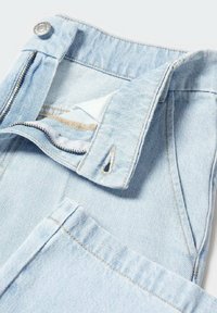 Los vaqueros de denim azul claro presentan un cierre de cremallera con un botón de metal. La tela tiene una textura sutil y costuras visibles en los bordes.