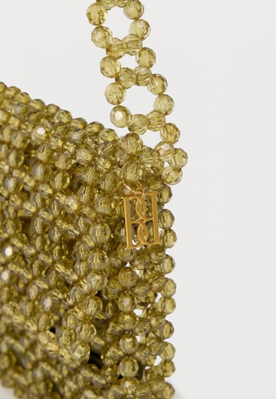 Κίτρινη ημιδιαφανής τσάντα με πολύεδρες χάντρες και χρυσό μενταγιόν με διασταυρωμένα αρχικά πάνω σε λευκό φόντο.