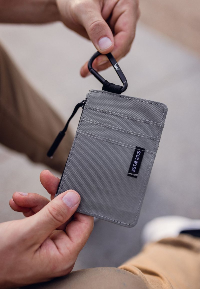 Gray fabric wallet with three card slots, a zip closure, and a black carabiner attachment. Neat stitching, durable material, and compact design.
