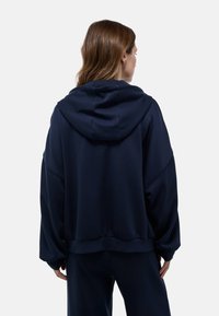 Sweatshirt à capuche bleu marine en tissu doux, avec une coupe décontractée, des épaules tombantes et un ourlet côtelé. Pas de motifs ou de matériel visible.