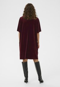 Rochie din catifea burgundy, cu mâneci scurte, design până la genunchi și o croială lejeră, asortată cu cizme negre lungi până la genunchi cu toc stiletto.