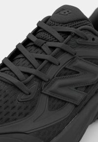 Chaussure de sport noire avec dessus en mesh, logo "N" bien visible et lacets plats. Dotée d'une languette rembourrée et de superpositions synthétiques pour le maintien.