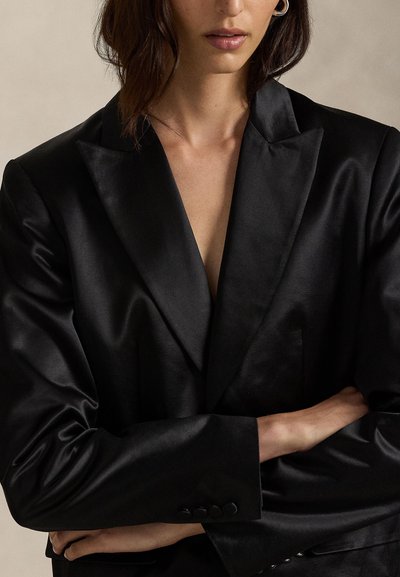 Blazer preto de cetim com decote em V profundo, ombros estruturados e textura suave. Apresenta detalhes de botões nas mangas.