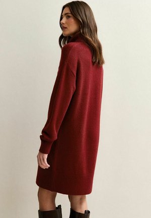 Vestido de punto, de manga larga y cuello alto en rojo profundo. Corte holgado con puños y dobladillo acanalados. Textura suave, diseño hasta la rodilla.
