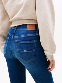 Blå denimjeans med en jevn tekstur, rett passform og en baklapp i brunt skinn. Har kontrasterende sømmer og en liten logo på baklommen.