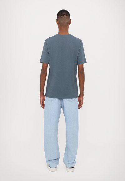 Grå t-shirt med korte ærmer og rund hals, parret med lys blå brede bukser. Stoffet ser blødt og afslappet ud.