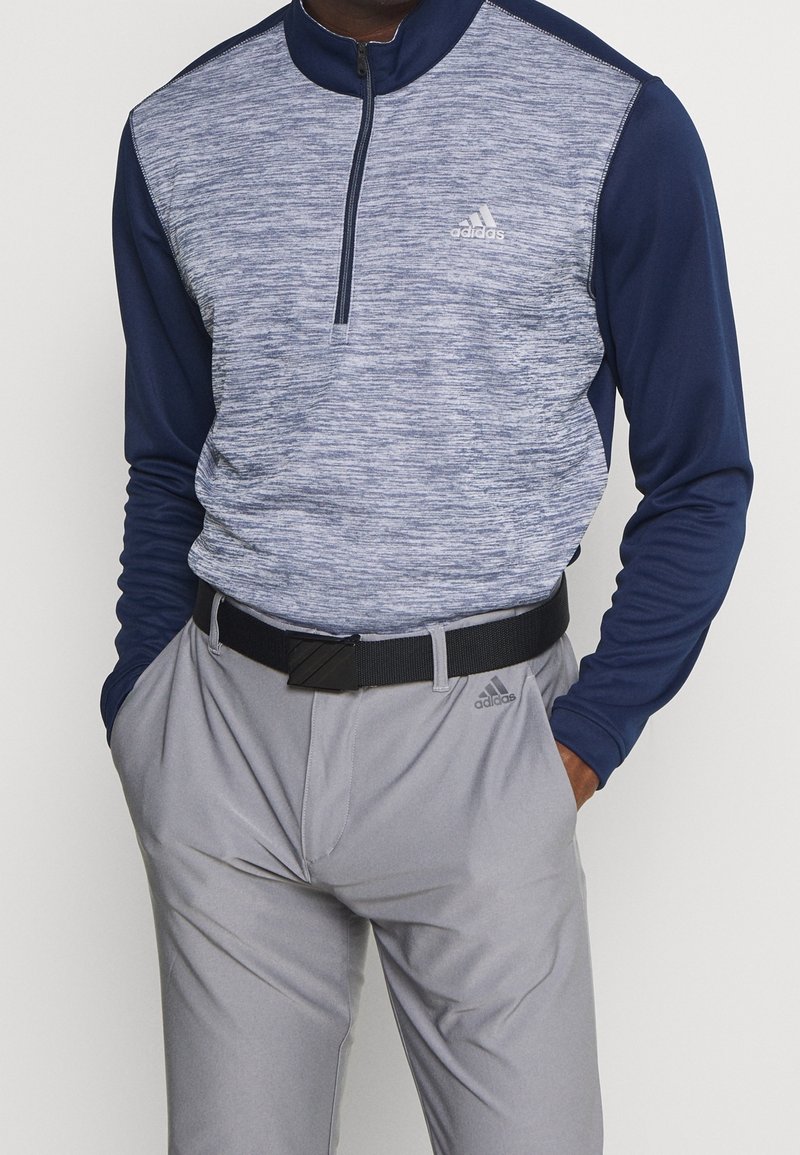 Pull-over à demi-fermeture éclair en tissu bleu chiné gris, avec manches longues. Associé à un pantalon gris et une ceinture noire avec boucle rectangulaire.