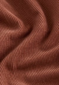 Tissu de couleur rouille avec une texture côtelée, comportant des lignes ondulées et une apparence douce et chaleureuse. Aucune motif ou accent visible.