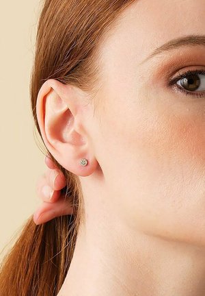 Silberne Steckerohrringe mit einem kreisförmigen Muster, die nah am Ohrläppchen befestigt sind. Glatte Textur, minimalistisches Design vor einem neutralen Hintergrund.