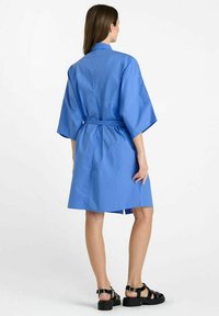 Vestido corto de manga corta en azul con un corte relajado, cinturón a la altura de la cintura y cuello con solapa. Confeccionado en una tela suave con una textura ligeramente brillante.