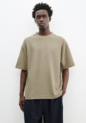 Khaki kortærmet struktureret t-shirt med rund hals, afslappet pasform og sideslidser, sat sammen med marineblå stribede bukser.