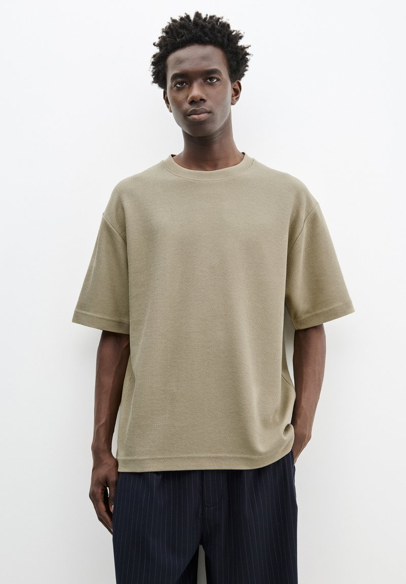 Khaki kortærmet struktureret t-shirt med rund hals, afslappet pasform og sideslidser, sat sammen med marineblå stribede bukser.