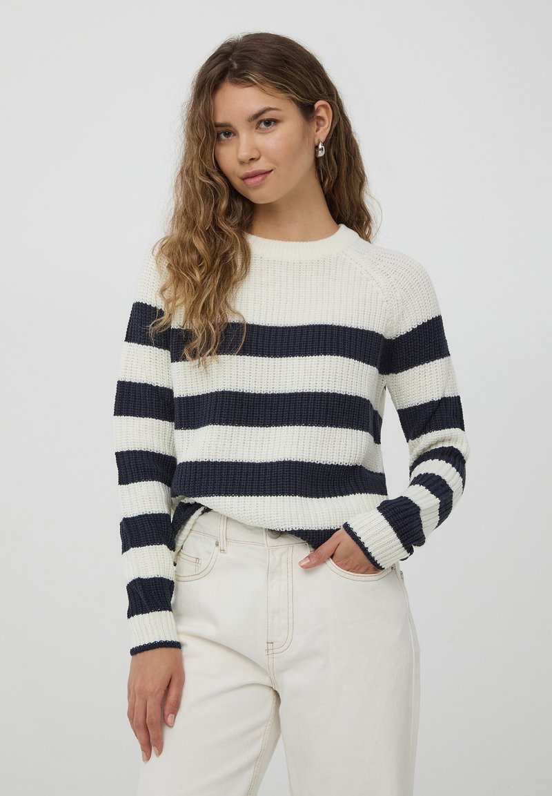 Maglione lavorato a maglia con strisce orizzontali blu navy e crema, colletto rotondo e polsini a coste; indossato sopra pantaloni chiari. La texture appare spessa.