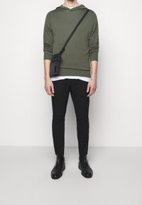Oliwkowy hoodie z sznurkiem, czarna torba na ramię, czarne dopasowane spodnie oraz czarne botki typu chelsea. Prosty design i tekstura materiału.