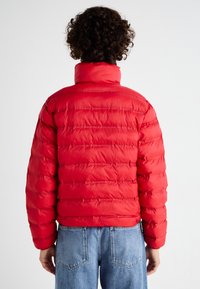 Rode pufferjack met een hoge kraag, gestikte design en elastische manchetten. Draagt over lichtblauwe denim jeans, wat een casual stijl laat zien.