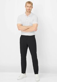 Witte polo met korte mouwen gecombineerd met zwarte, nauwsluitende broek en witte sneakers. Soepele stof, kraag met knopen en een getailleerd ontwerp.