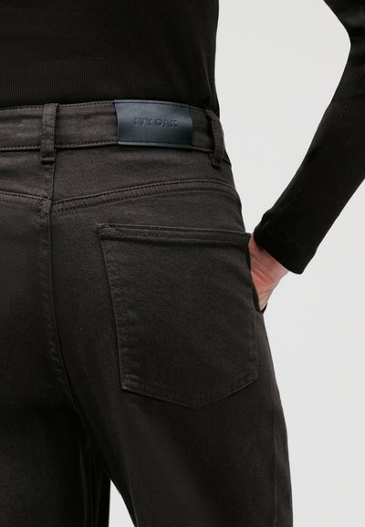 Pantaloni in denim neri con una trama liscia, dotati di un'etichetta in pelle in vita e un classico design a cinque tasche.