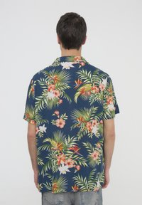 Camicia a maniche corte con bottoni in tessuto blu scuro, impreziosita da un vivace motivo floreale tropicale che presenta foglie di palma e fiori di ibisco.