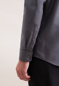 Camicia a maniche lunghe di colore grigio scuro con un motivo geometrico. Presenta polsini con bottoni e una texture sottile. Design ben sagomato e forma su misura.