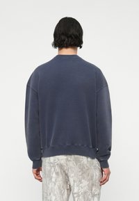 Ναυτικό μπλε φούτερ με στρογγυλή λαιμόκοψη, κατεβασμένους ώμους και ριγωτούς μανικιούδες. Μαλακό, υφασμάτινο ύφασμα και χαλαρή γραμμή.