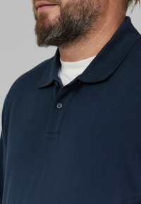 Granatowa polo wykonana z teksturowanej tkaniny, z kołnierzykiem zapinanym na guziki, krótkimi rękawami oraz małym haftowanym logo na piersi.