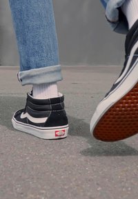 Schwarze High-Top-Sneaker mit weißen Akzenten, aus strukturiertem Wildleder, einer Gummisohle mit Diamantmuster und sichtbarem Logo an der Ferse.