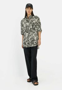 Zwart-wit blouse met een bladpatroon en een relaxte pasvorm, gecombineerd met losse zwarte broek en zwarte sandalen.
